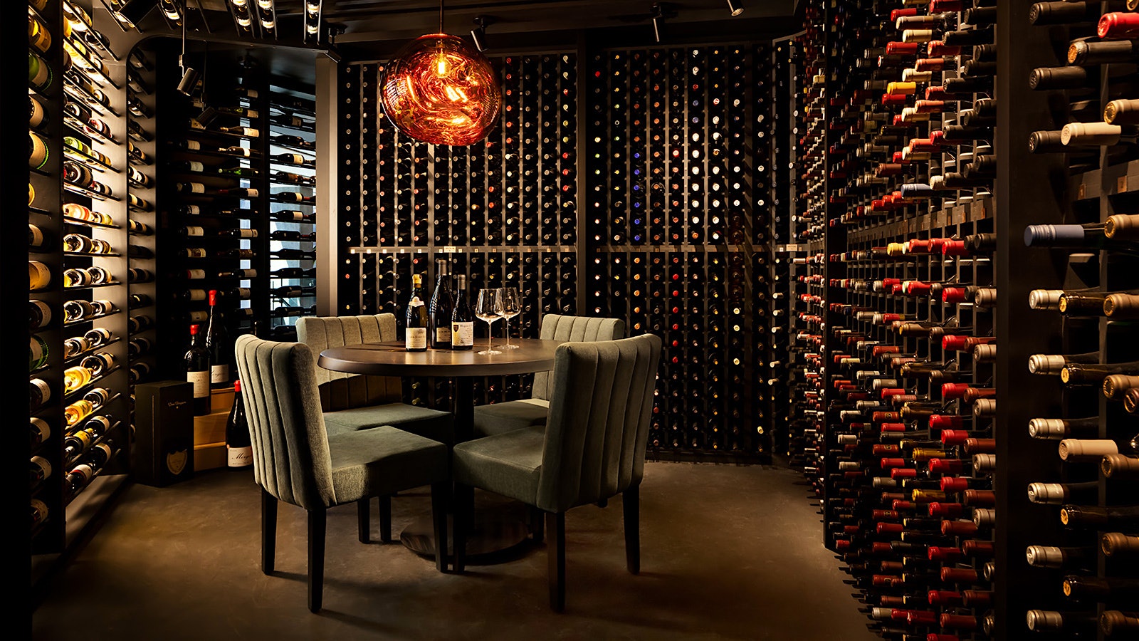 A table set with wineglasses and bottles with four gray chairs in the cellar of Restaurant h3